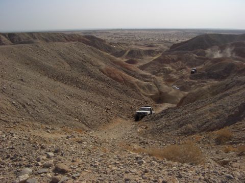 1985 Ford Bronco - Off-road vehicles descend into a desert canyon, kicking up dust on the trail.