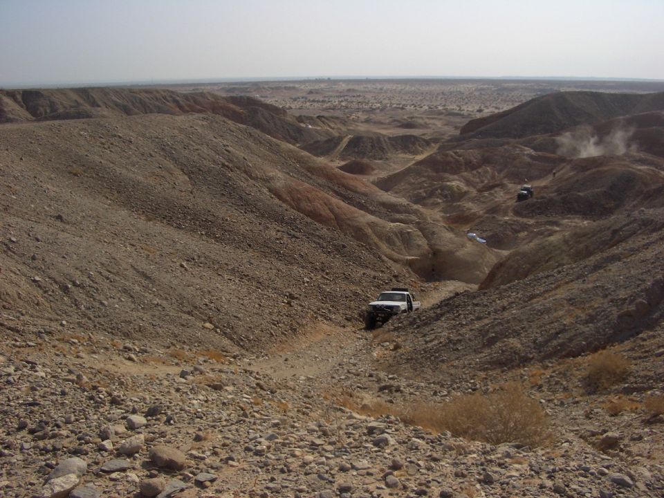 Several off-road vehicles navigate a rocky, dry canyon under a hazy sky