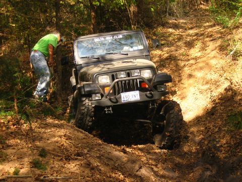 2001 Jeep Wrangler - A Jeep Wrangler is shown on a muddy, wooded trail with a person assisting.