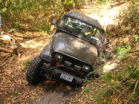 2001 Jeep Wrangler - A dark Jeep Wrangler is shown navigating a challenging muddy off-road trail, with text visible on its windshield.