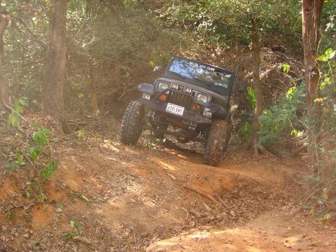 2001 Jeep Wrangler - A Jeep Wrangler navigates a steep, wooded trail, kicking up dirt as it descends.