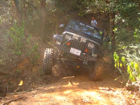 2001 Jeep Wrangler - A black Jeep Wrangler navigates a steep, wooded trail with a person standing in the background.