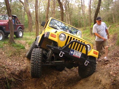 2001 Jeep Wrangler - A yellow 2001 Jeep Wrangler is shown navigating a challenging off-road trail with another Jeep visible in the background.