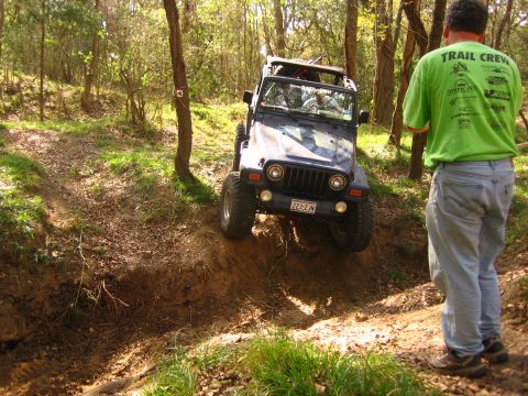 2001 Jeep Wrangler - A dark blue Jeep Wrangler navigates a steep, muddy trail in a wooded area.