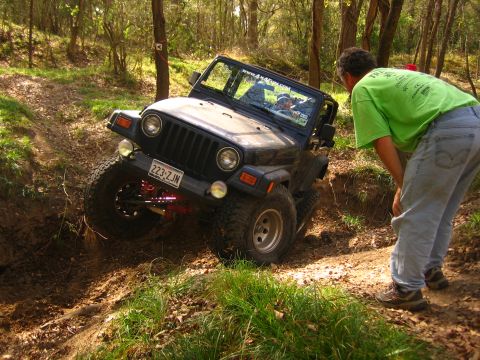 2001 Jeep Wrangler - A black 2001 Jeep Wrangler navigates a steep, muddy incline on a wooded trail, with a person observing the off-road maneuver.