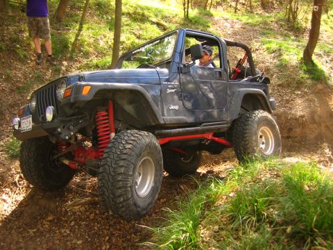2001 Jeep Wrangler - A blue Jeep Wrangler navigates a wooded trail with its top removed and suspension modified for off-road use.