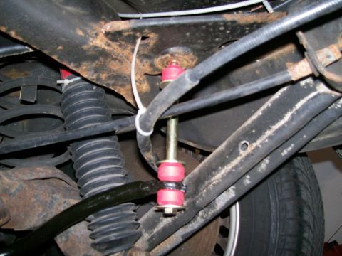 1995 Mercury Grand Marquis - Close-up of the rear sway bar components, showing red bushings and a yellow bolt against a rusty frame.