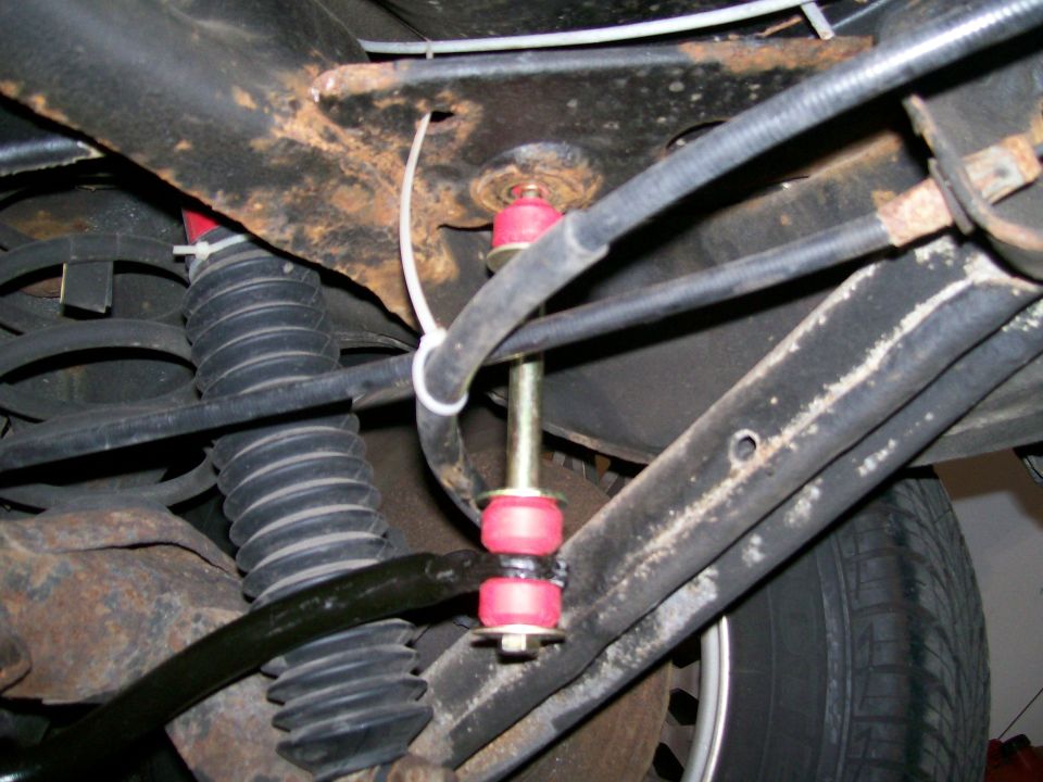 Rear sway bar with red bushings and yellow bolt, attached to rusty frame and black coil spring