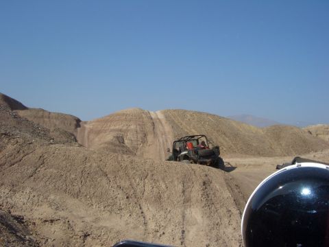 1985 Ford Bronco - Two off-road vehicles navigate a dusty, hilly terrain on a clear day.