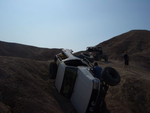 1985 Ford Bronco - Two off-road vehicles navigate a steep, dusty terrain under a clear blue sky.
