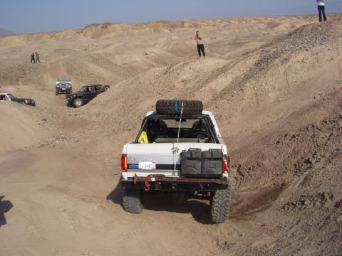 1985 Ford Bronco - Multiple off-road vehicles navigate a sandy desert terrain, with a 1985 Ford Bronco in the foreground.