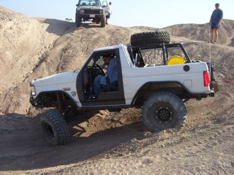 1985 Ford Bronco - A modified white SUV navigates a steep, sandy incline with another vehicle visible in the background.