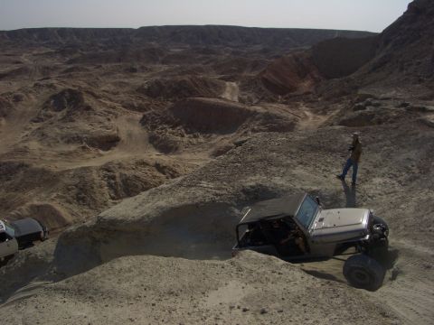 1985 Ford Bronco - Multiple off-road vehicles traverse a challenging desert landscape with steep inclines and rocky formations.
