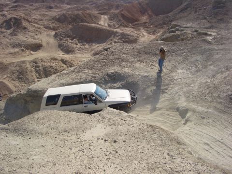 1985 Ford Bronco - A white SUV tackles a challenging off-road course in a barren, desert landscape.