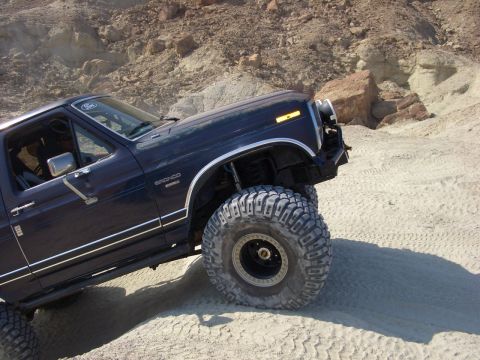 1985 Ford Bronco - 1985 Ford Bronco navigates a rocky desert terrain with its large tires.