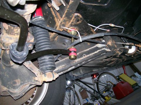 1995 Mercury Grand Marquis - Underside view of a car's front suspension in a garage showing a black sway bar with a new end link fitted with red polyurethane bushings,…