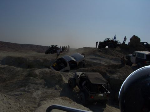 1985 Ford Bronco - Multiple off-road vehicles traverse a challenging, dusty landscape, with one vehicle appearing to be stuck or tilted.