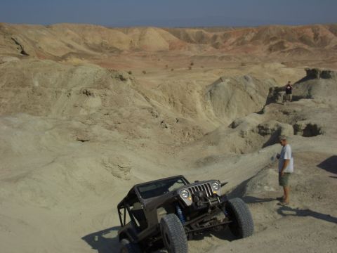 1985 Ford Bronco - A modified Jeep navigates a sandy, hilly terrain under a clear blue sky.