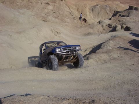 1985 Ford Bronco - Customized pickup truck navigates a steep, sandy incline in a desert landscape.