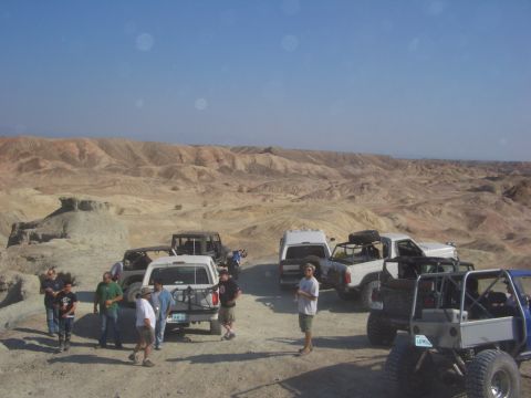 1985 Ford Bronco - Several off-road vehicles are parked in a desert landscape with a group of people gathered around.