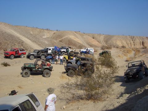 1985 Ford Bronco - A group of off-road vehicles gathered in a dry, hilly desert environment under a clear blue sky.
