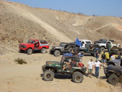 1985 Ford Bronco - A group of off-road vehicles, including a red 1985 Ford Bronco, gather in a desert landscape.