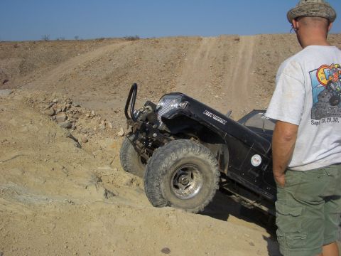 1985 Ford Bronco - A man watches an off-road vehicle ascend a challenging dirt incline in a desert landscape.