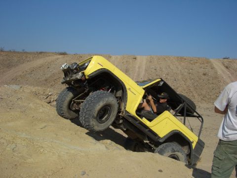 1985 Ford Bronco - A yellow Bronco navigates a steep dirt incline under a clear blue sky.