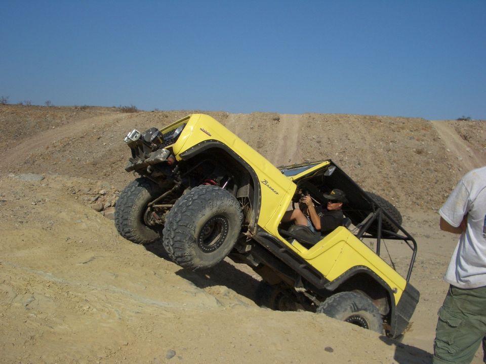 Yellow off-road vehicle with large tires climbing a dirt hill. "Bronco" text visible on the side