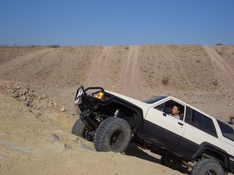 1985 Ford Bronco - A modified SUV navigates a steep, sandy incline under a clear blue sky.