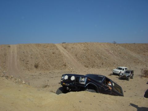 1985 Ford Bronco - Multiple off-road vehicles navigating challenging sandy terrain under a clear blue sky.