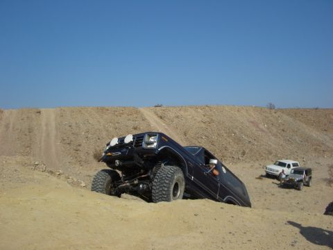 1985 Ford Bronco - An off-road SUV navigates a steep sandy incline, with two other vehicles visible in the background.