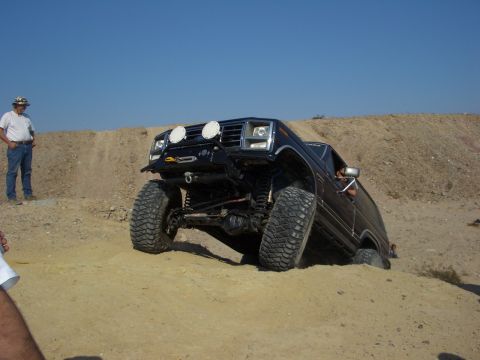 1985 Ford Bronco - A modified Ford Bronco navigates a steep dirt incline under a clear blue sky.