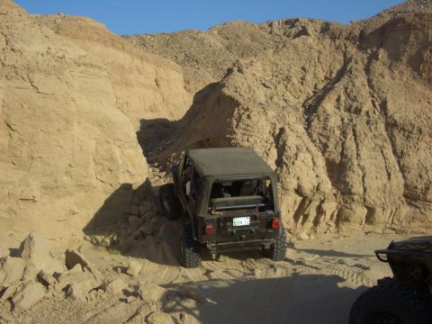 1985 Ford Bronco - A Jeep Wrangler navigates a narrow canyon trail, with another vehicle partially visible in the foreground.