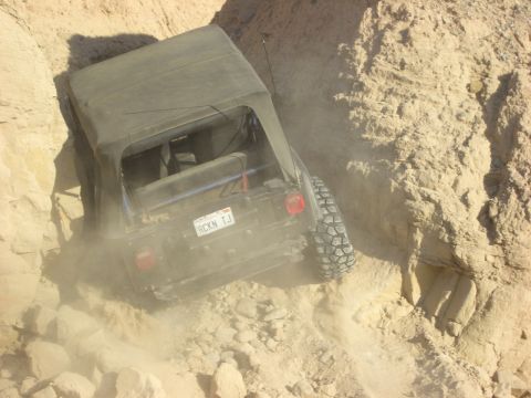 1985 Ford Bronco - A Jeep Wrangler TJ navigates a challenging off-road trail, its tires kicking up dust as it descends a steep embankment.