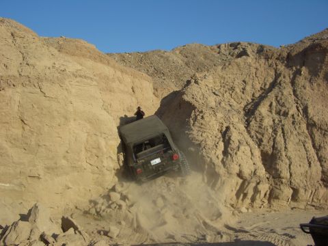1985 Ford Bronco - An off-road vehicle navigates a steep, sandy terrain in a desert canyon.