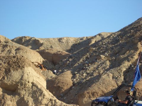 1985 Ford Bronco - A rusted car wreck is visible in a desert ravine, while a blue off-road vehicle drives nearby.