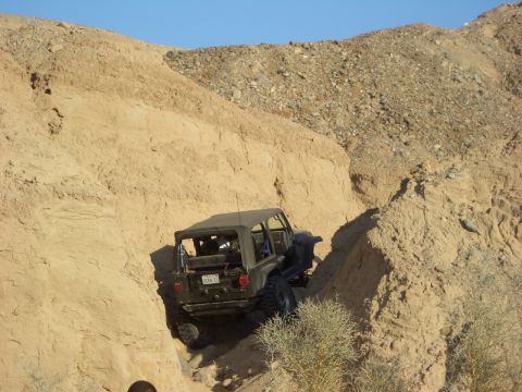 1985 Ford Bronco - A black Jeep Wrangler TJ maneuvers through a tight off-road trail in a desert canyon.