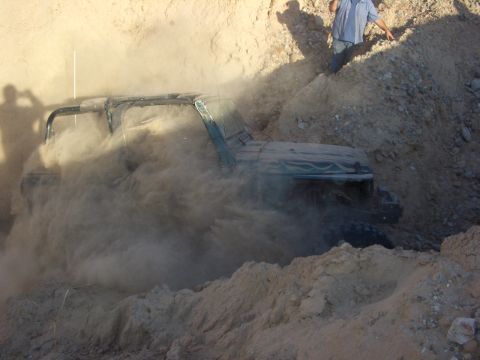 1985 Ford Bronco - An off-road vehicle is partially submerged in loose dirt, creating a cloud of dust.