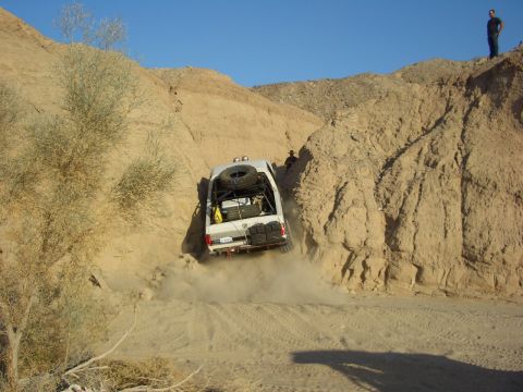 1985 Ford Bronco - A white 1985 Ford Bronco navigates a challenging descent on a dusty, off-road trail.