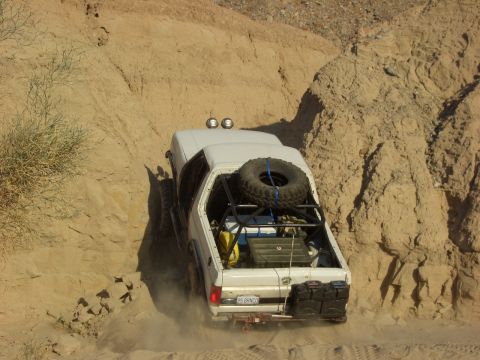 1985 Ford Bronco - A white pickup truck navigates a steep, dusty off-road trail.