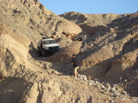 1985 Ford Bronco - Two off-road vehicles navigate a steep, rocky canyon under a clear blue sky.