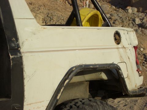 1985 Ford Bronco - Rear view of a 1985 Ford Bronco showing the quarter panel, roll cage, and a yellow item in the cargo area.