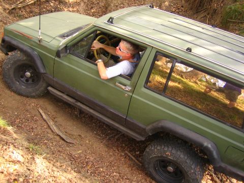 2001 Jeep Wrangler - A green Jeep Cherokee XJ navigates an off-road trail, its driver visible through the window.