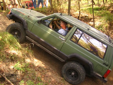 2001 Jeep Wrangler - A green Jeep Cherokee navigates a steep dirt path during an off-road excursion, with other vehicles and people visible in the background.