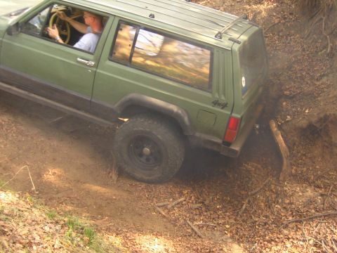 2001 Jeep Wrangler - A green Jeep Cherokee XJ navigates a steep dirt path with fallen leaves and branches.