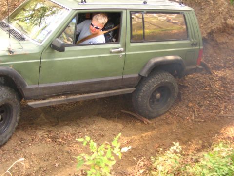 2001 Jeep Wrangler - A driver navigates a green Jeep Cherokee XJ over rough, wooded terrain.