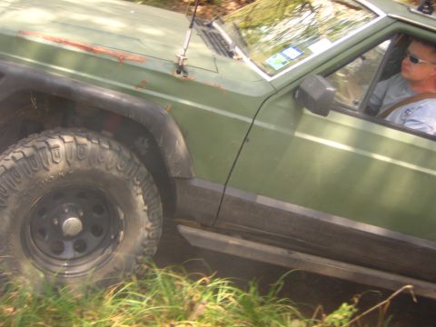 2001 Jeep Wrangler - A green Jeep Cherokee with off-road tires is driven by a man wearing sunglasses.