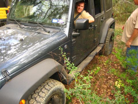 2001 Jeep Wrangler - A man smiles from inside a dark gray Jeep Wrangler as it sits off-road, with another vehicle partially visible.