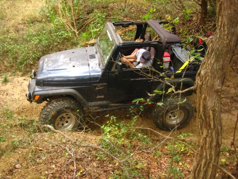 2001 Jeep Wrangler - A black Jeep Wrangler navigates an off-road trail, with its tires digging into the dirt as it drives through a wooded area.